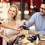 Happy couple using smart phone for contactless payment in a restaurant.