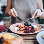 Breakfast and Brunch Chain Grew Sales per Household 8.63% with Valpak Diner cutting into a stack of blueberry pancakes with berry sauce and whipped cream at a brunch restaurant table