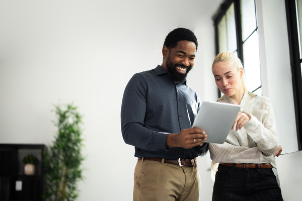 Two diverse business colleagues collaborating and smiling while viewing a digital tablet