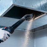 259243434 - a glove hand uses a vacuum hose to clean a dirty air duct, removing dust and particles