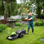 Professional gardener mows the lawn with a mower in beautiful private house garden.